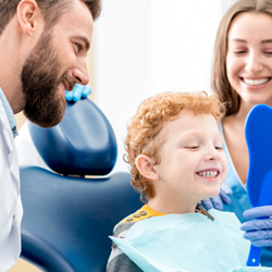 Child smiling at reflection with dentist and assistant